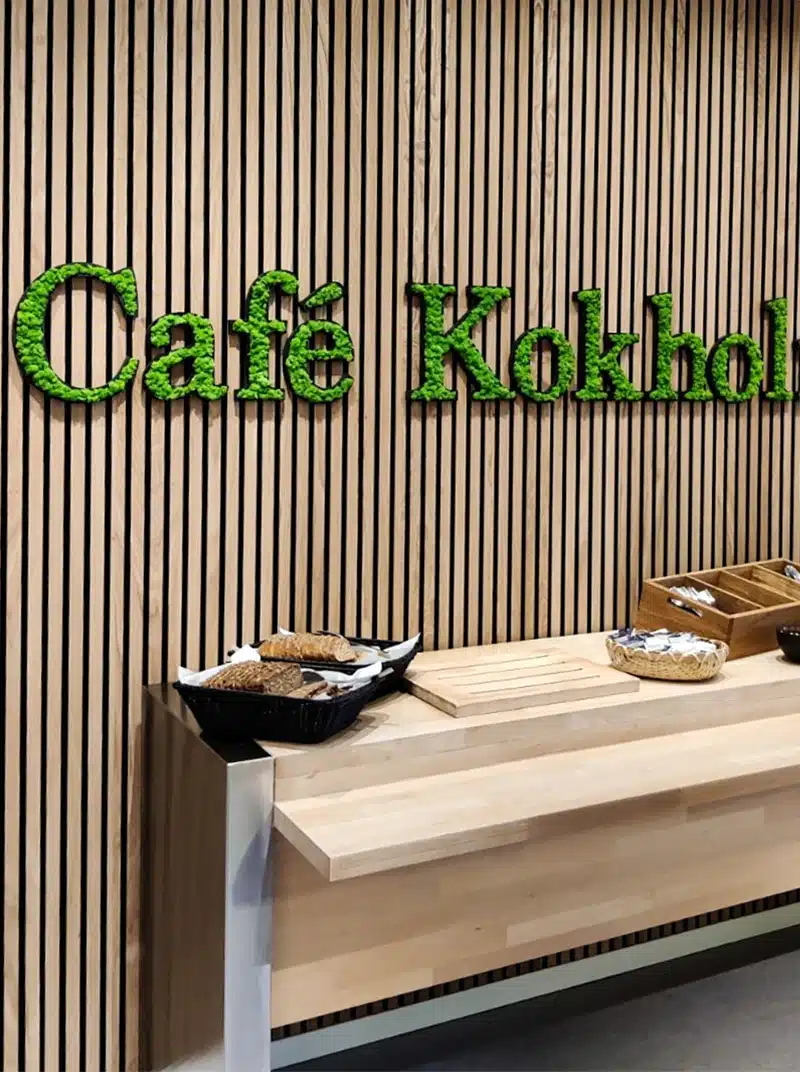 Semnul Café Kokholma pe perete de lemn, cu produse de patiserie.